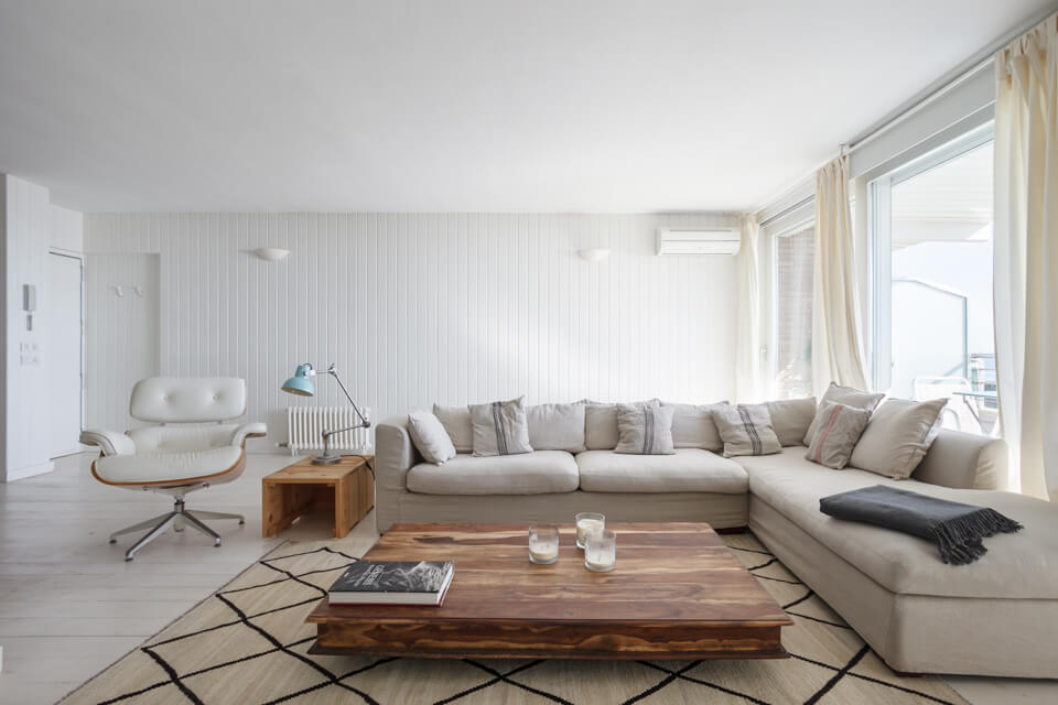 Salón de apartamento turístico en Gavà decorado en colores crema con sofà esquinero, sillón de piel y mesa de madera maciza