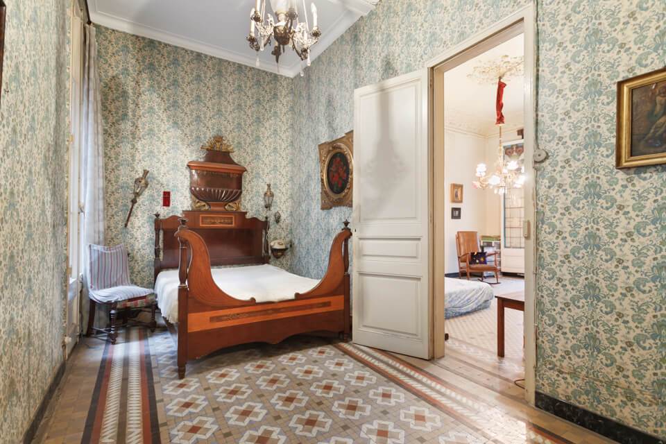 Dormitorio con cama doble de madera maciza, papel pintado y suelo hidraulico en apartamento del Eixample de Barcelona.