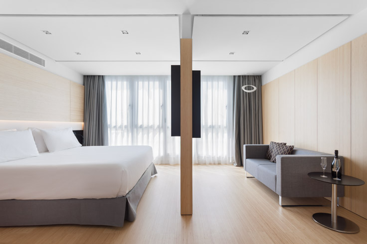 Plano conjunto de la zona de dormitorio y el salón con televisión de la habitación piloto del nuevo hotel del Grupo Hotusa en la Ronda Universitat de Barcelona