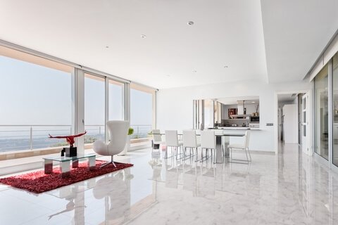 Portada de la galería casas. Fotografía de salón comedor de casa costera con mesa de cristal, sillas de piel, sillón y escultura frente a una terraza con vistas al mar.