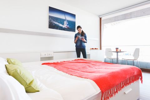 Portada de la galería del proyecto fotográfico Ghosts. Fotografía de una mujer leyendo un catálogo en mitad de una habitación de hotel.