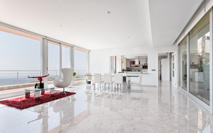 Portada de servicios de fotografía de interiores. Salón comedor de casa costera con mesa de cristal, sillas de piel, sillón y escultura frente a una terraza con vistas al mar.